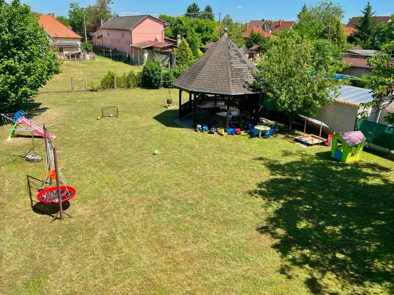 A vendégház nagy füves kertje filagóriával és játszórésszel